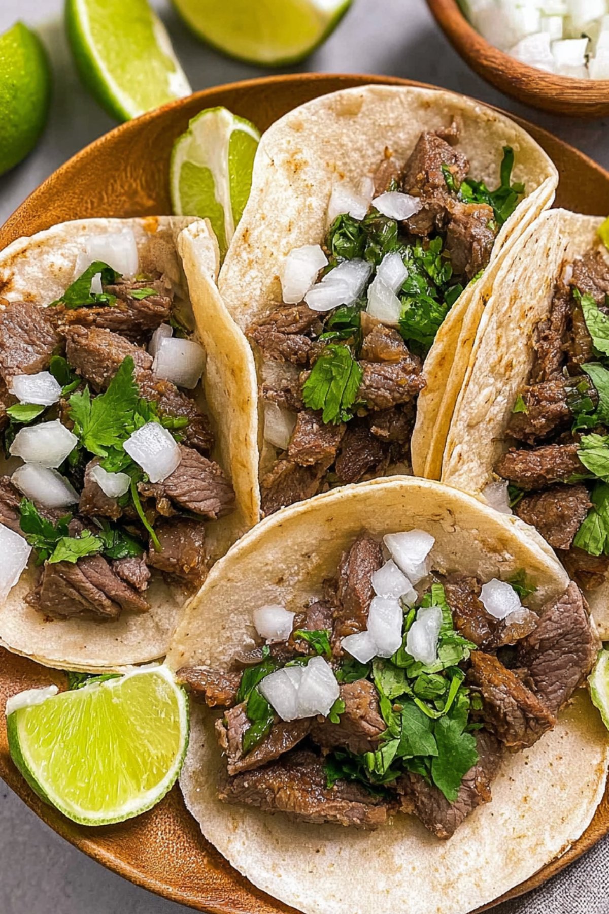 Overhead view of a wooden bowl filled with street style steak tacos garnished with cilantro and diced onion