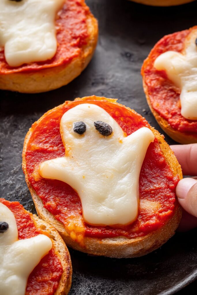 Close-up of ghost-shaped cheese on mini pizza with marinara sauce, a fun Halloween-themed recipe.