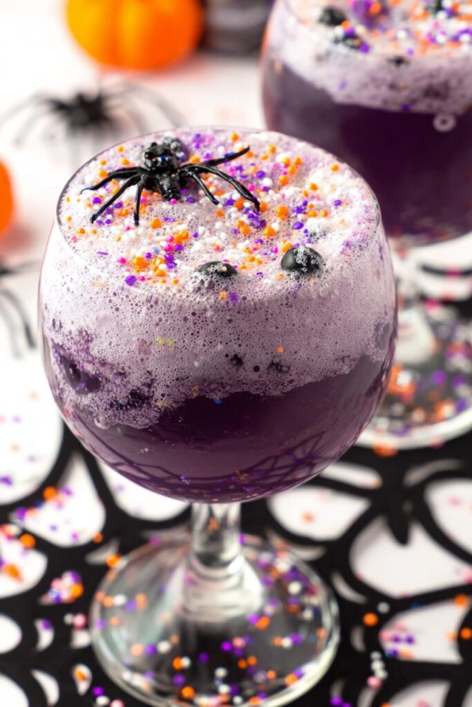 Foamy purple Halloween punch topped with Halloween sprinkles and a plastic spider decoration.