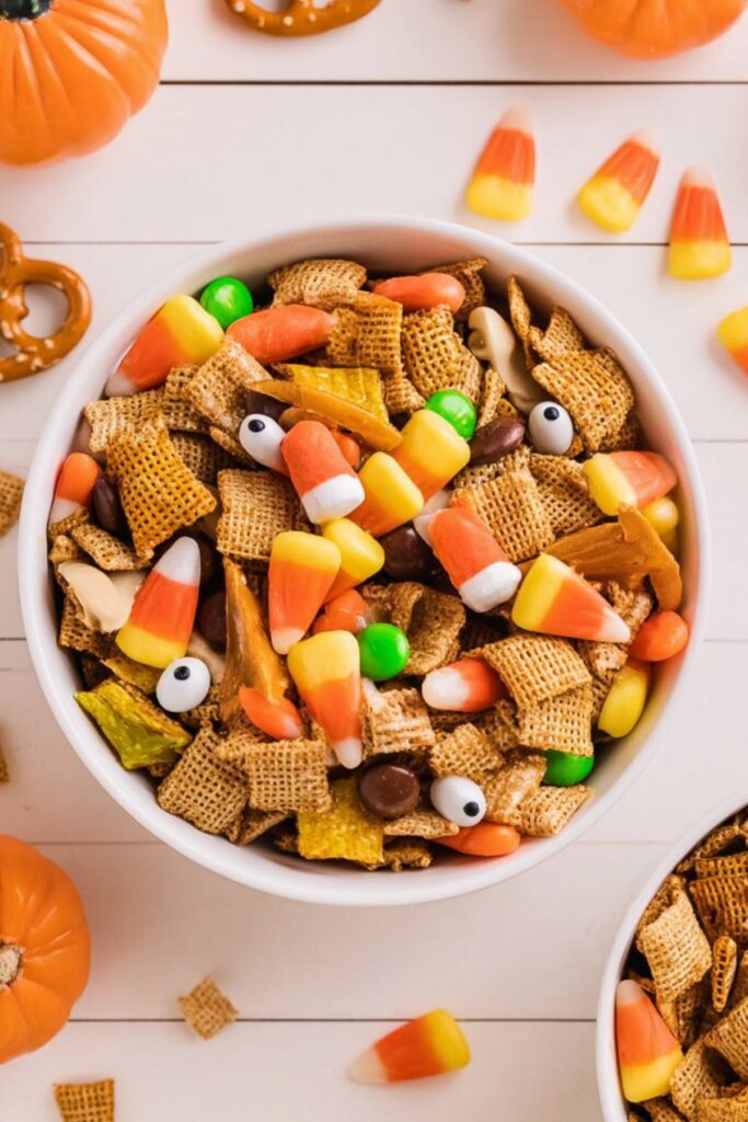 Halloween snack bowl with crunchy cereal mix, pretzels, candy corn, chocolate candies, and edible eyeballs for a party.