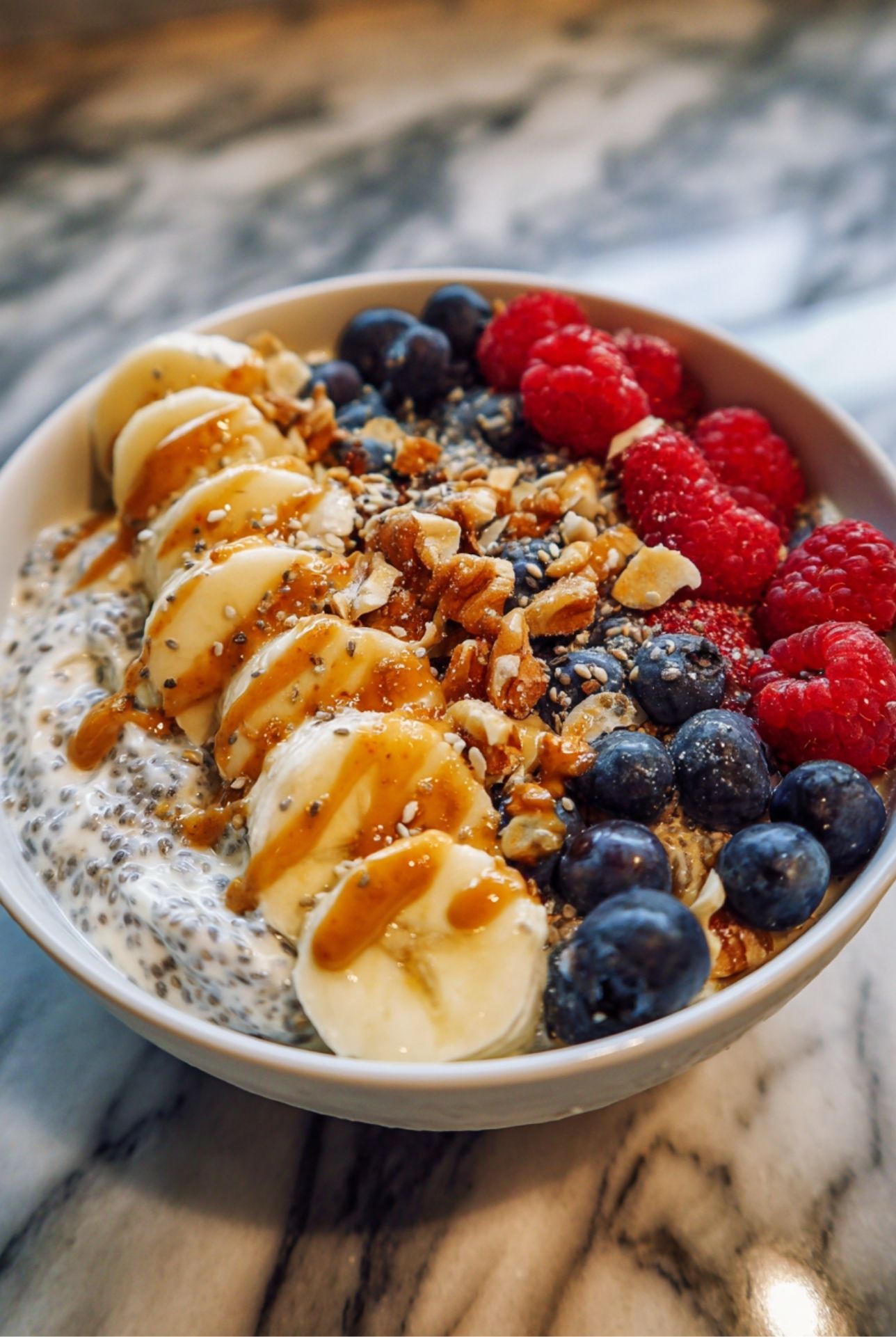 Healthy breakfast bowl made with chia pudding, banana slices, blueberries, raspberries, and crunchy nuts, drizzled with nut butter for protein and fiber.