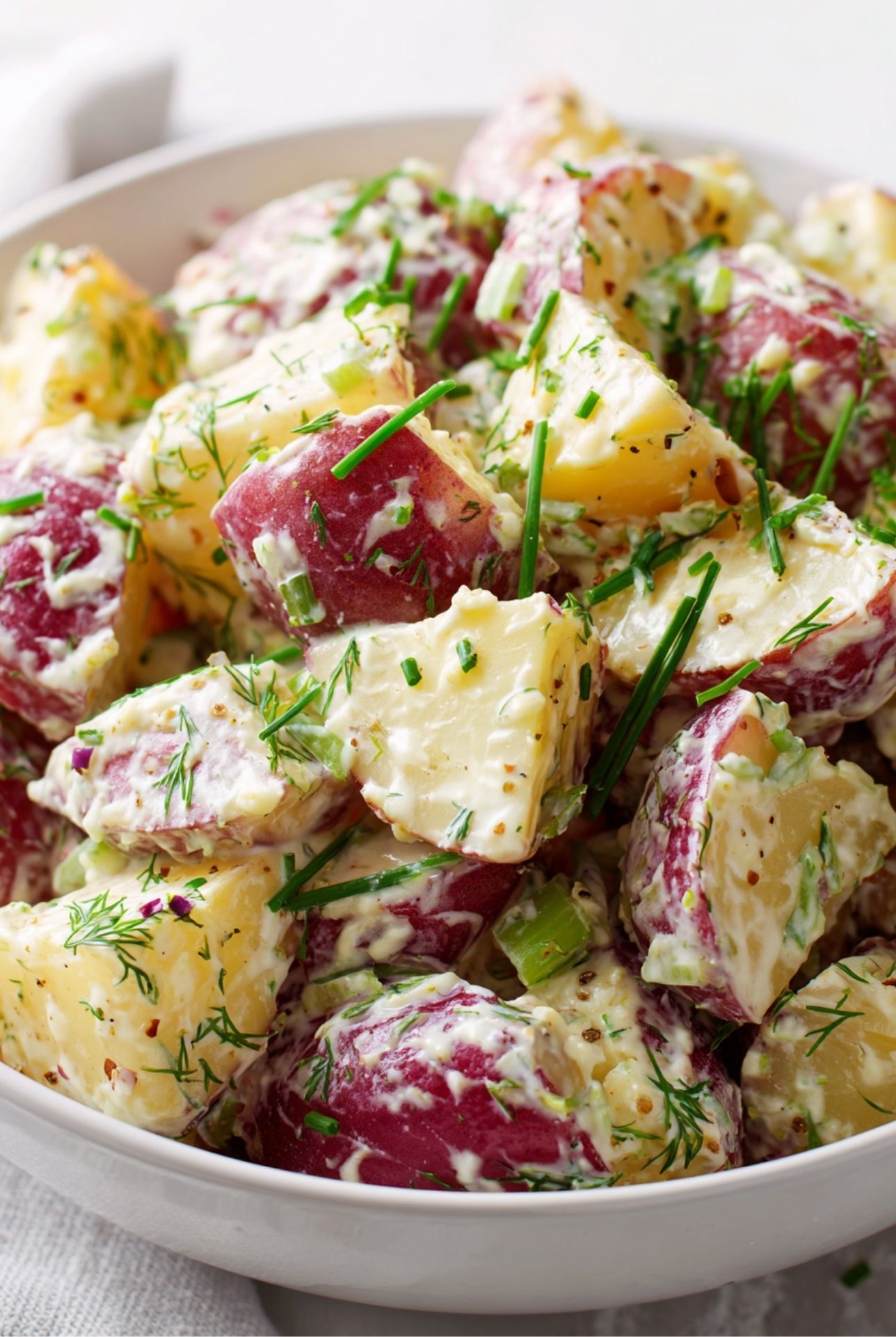 Red potato salad with creamy mustard dressing, garnished with fresh dill and scallions.