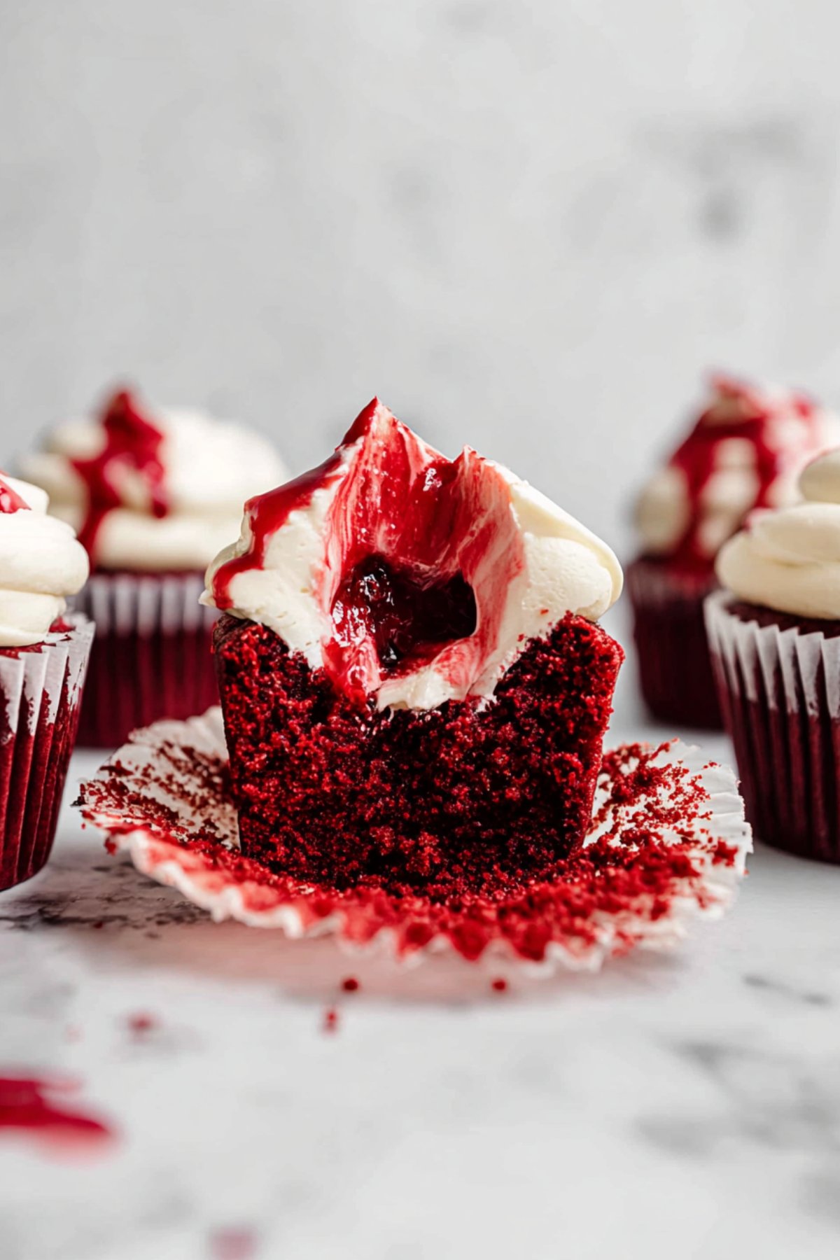 Close-up of a Halloween red velvet cupcake with cream cheese frosting and raspberry “blood” filling oozing from the center.