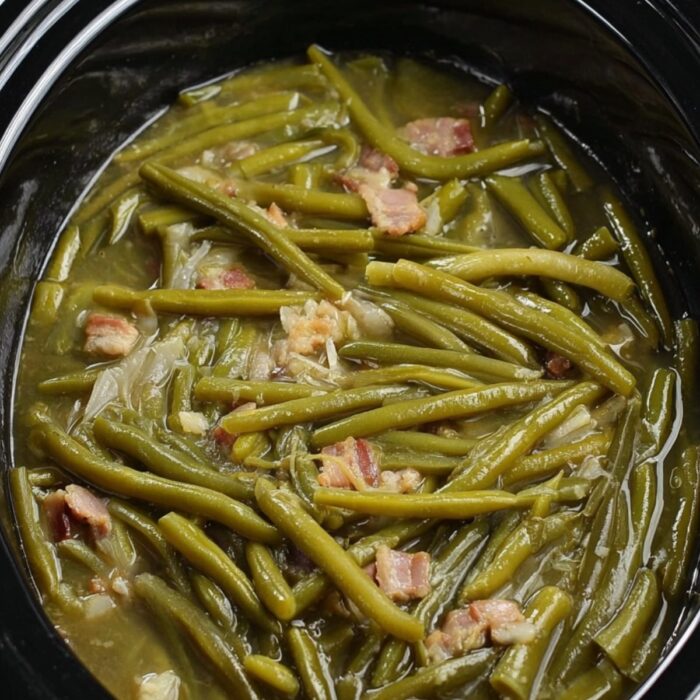 Slow cooker filled with green beans and bacon pieces in savory broth, cooked until tender.