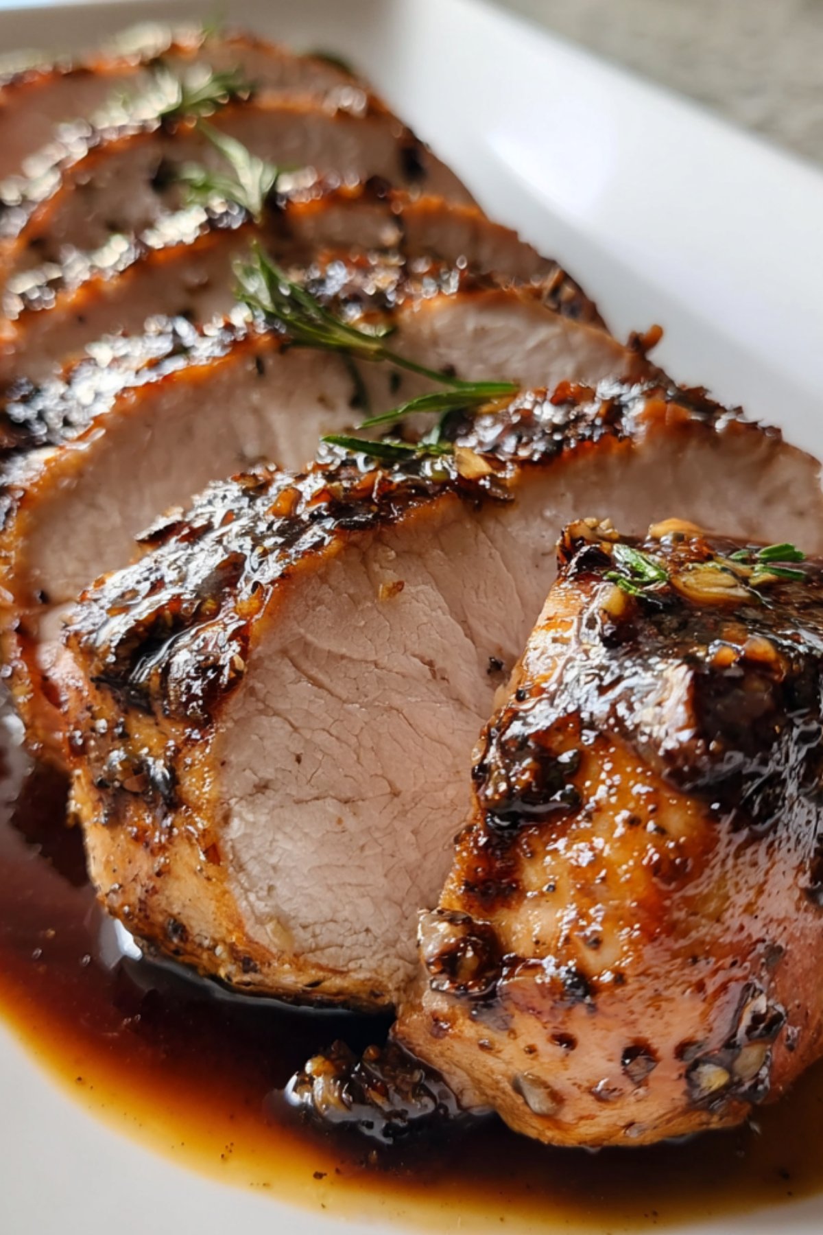 Pork loin roast sliced and served with gravy on a large white platter.