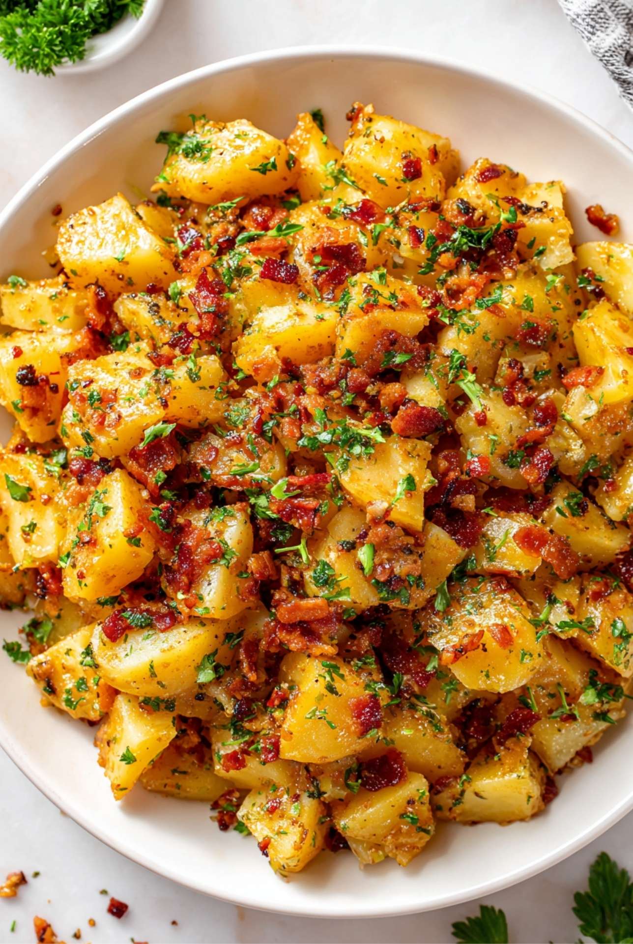 Overhead view of warm German potato salad with bacon crumbles and fresh herbs.