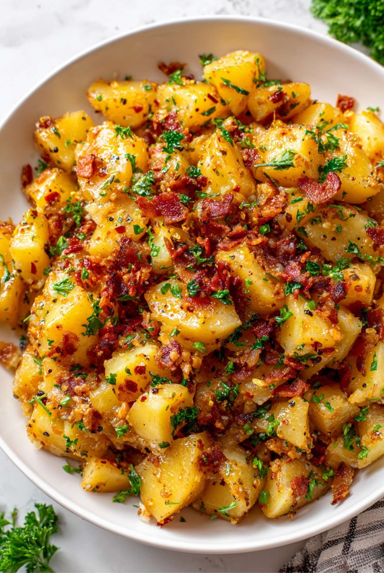 Serving bowl filled with warm German potato salad topped with bacon and parsley.
