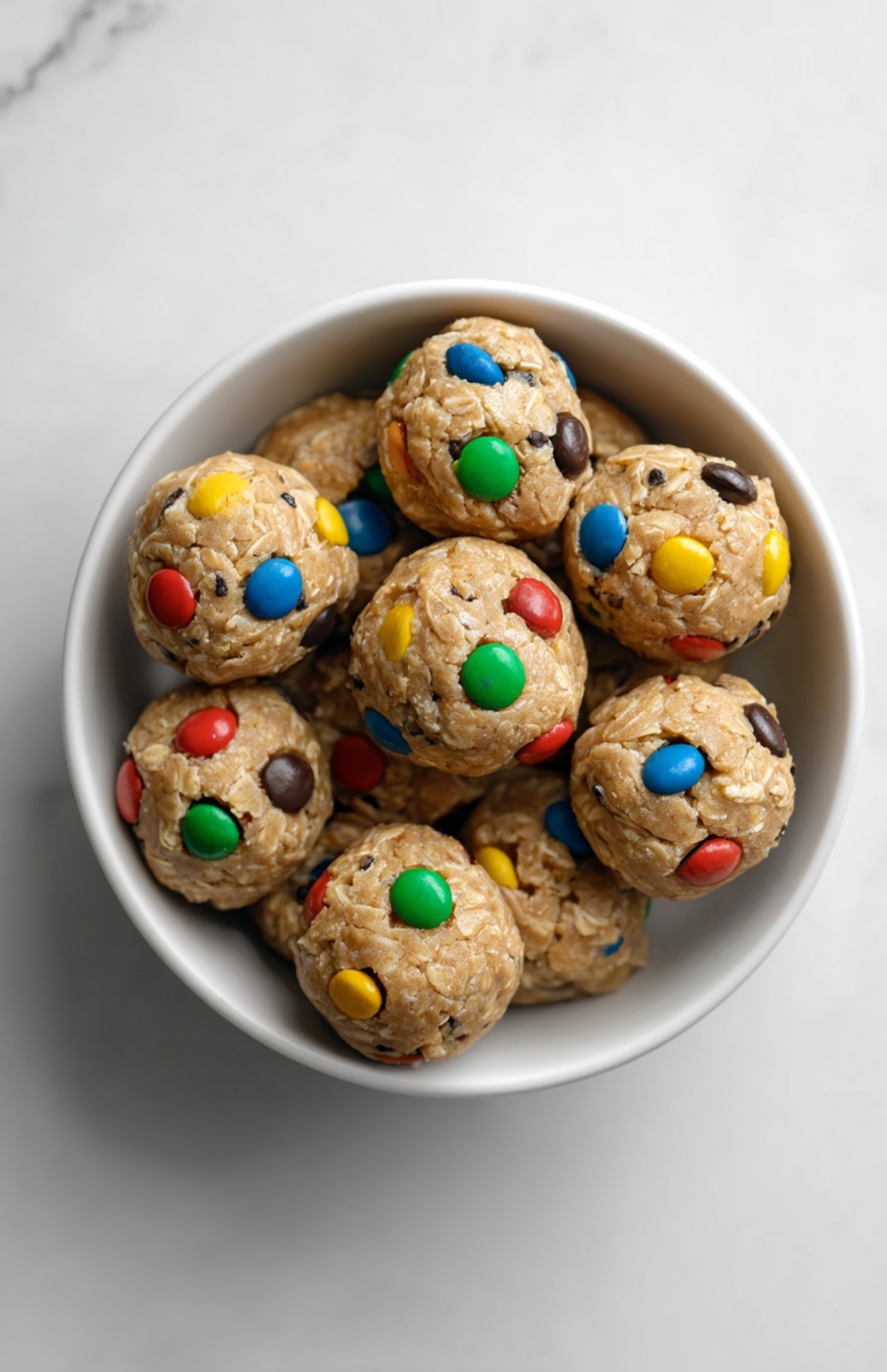 Bowl of peanut butter cookie protein balls with colorful M&Ms, stacked and ready to eat.