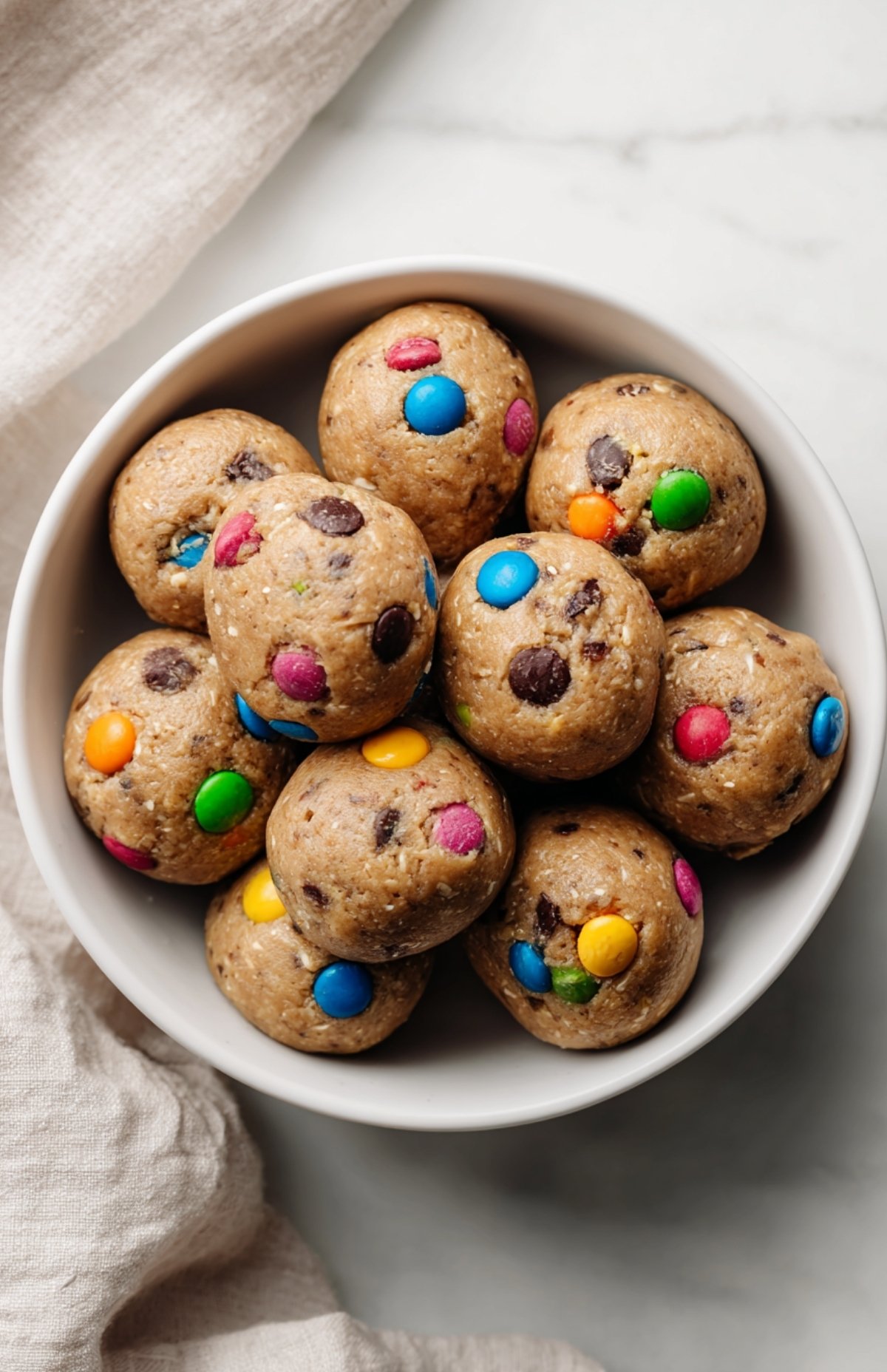 Glass storage container filled with colorful M&M cookie protein balls ready for fridge storage.