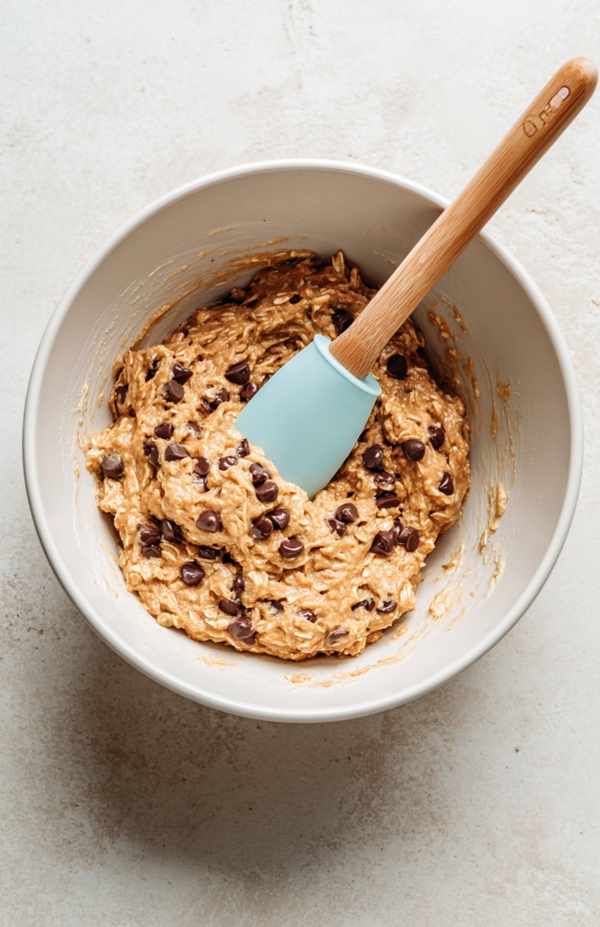 Mixing bowl filled with protein energy ball dough with chocolate chips and spatula.