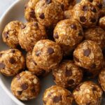 Close-up shot of no bake protein balls stacked in a bowl with oats and chocolate chips visible.