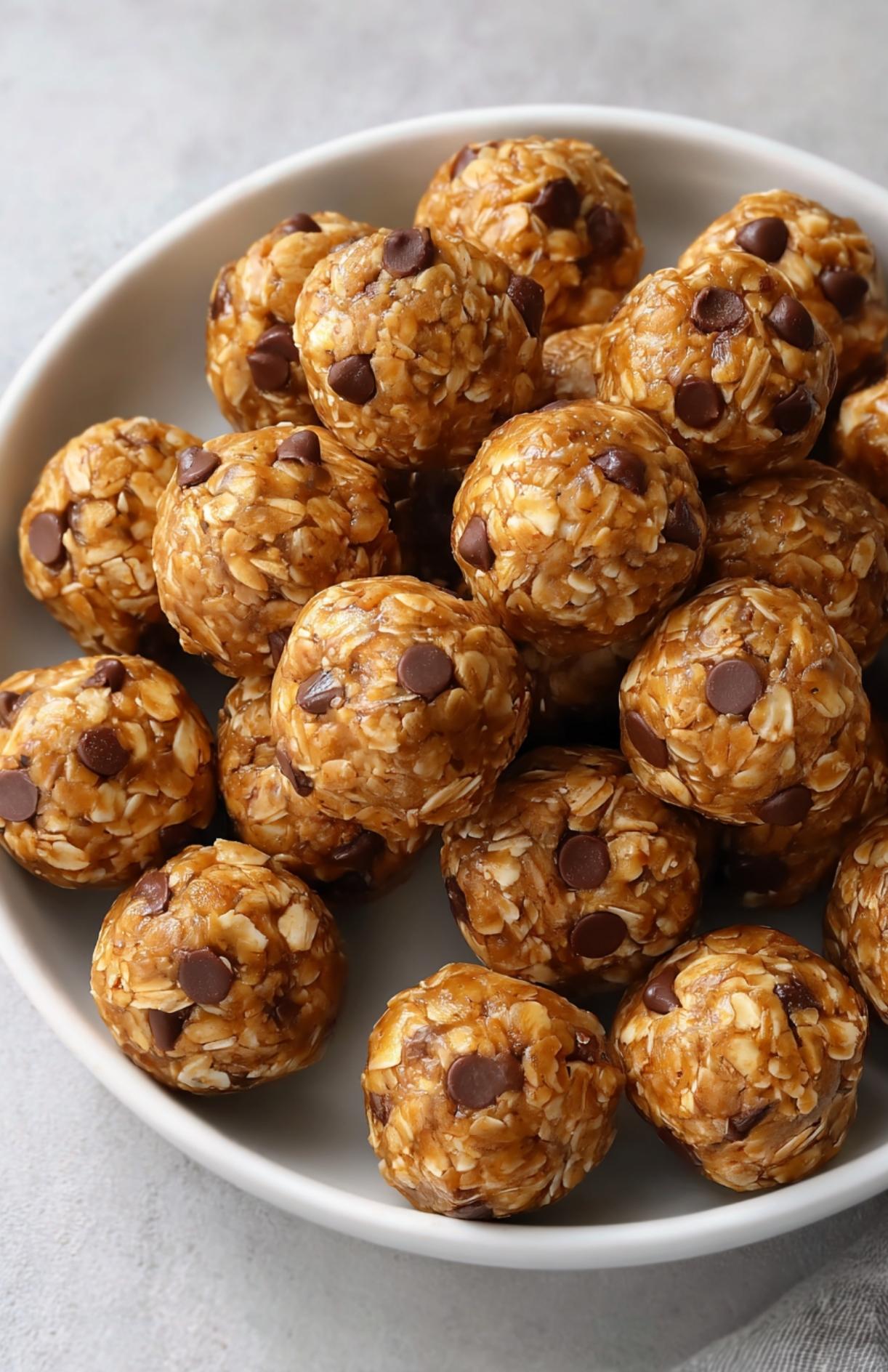 Close-up shot of no bake protein balls stacked in a bowl with oats and chocolate chips visible.