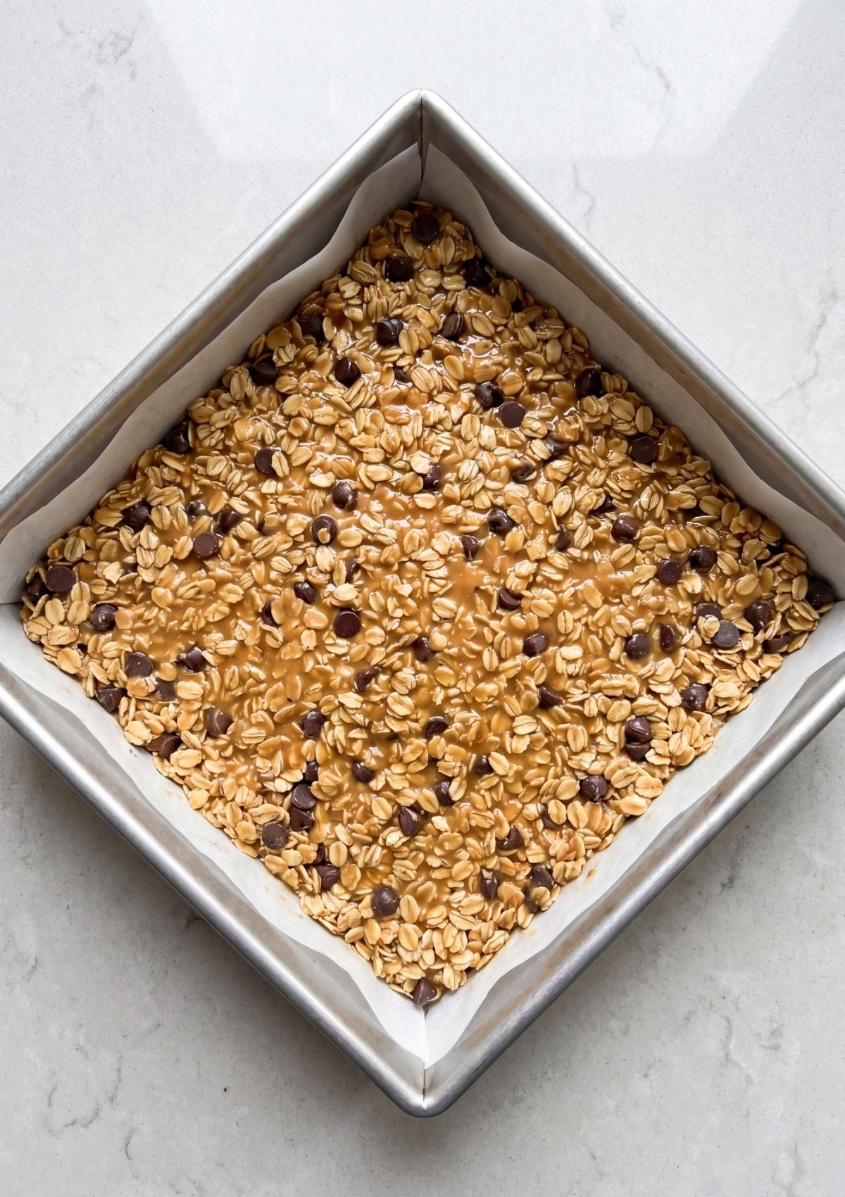 peanut butter oatmeal bars mixture spread in pan with chocolate chips before chilling and cutting