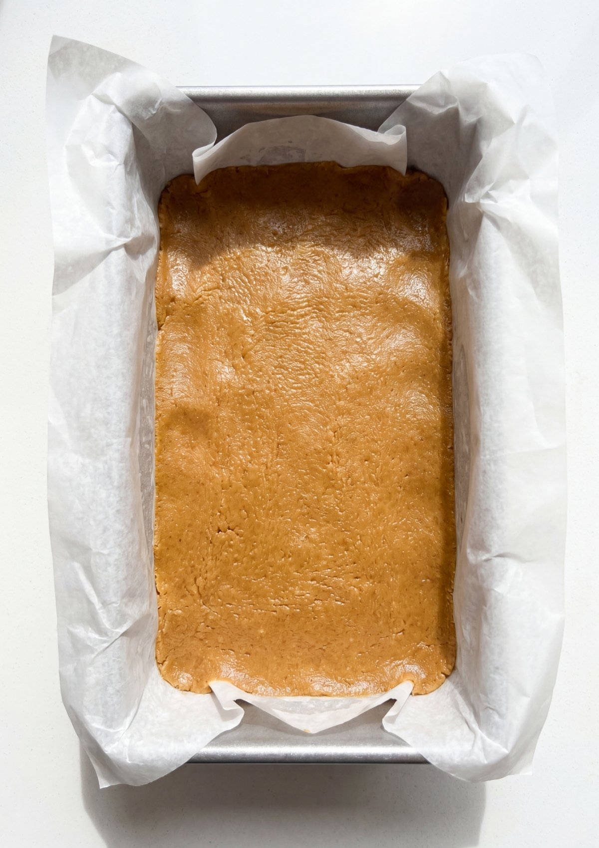 spreading melted chocolate over no bake protein bars in pan easy step