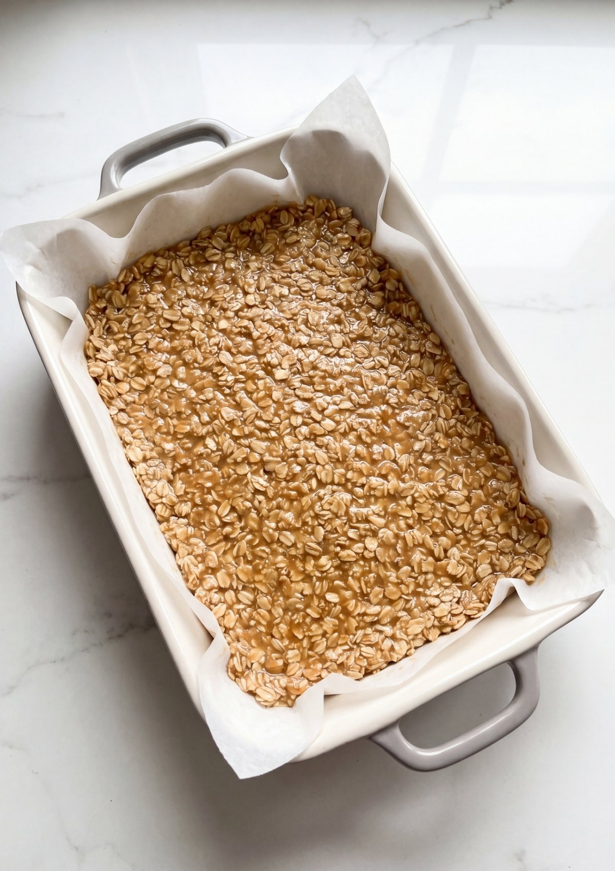 No Bake Oatmeal Bars mixture pressed into baking dish with parchment paper for quick meal prep snack