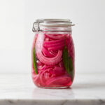 Sliced red onions and green chilis soaking in pink vinegar liquid inside a sealed glass jar