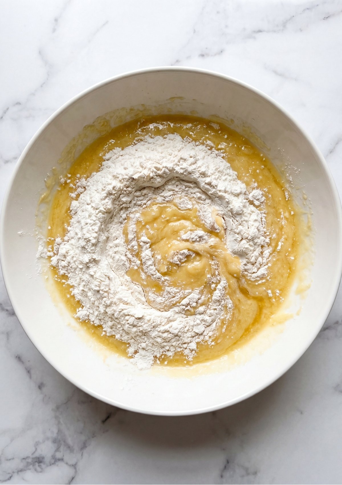 A white mixing bowl containing cookie dough being combined with all purpose flour