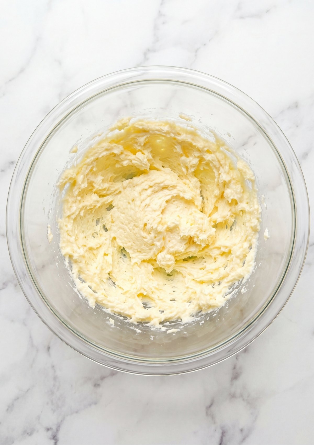 Creamed butter and sugar mixture beaten until light and fluffy inside a clear glass mixing bowl.