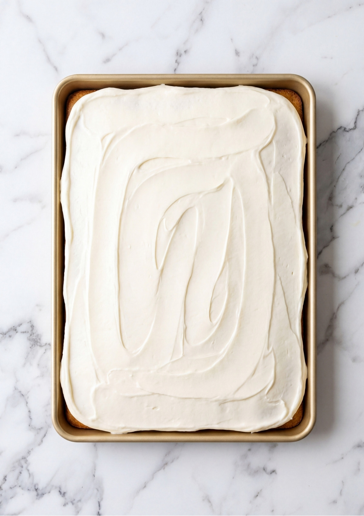 A golden sheet cake in a baking pan completely covered in a smooth layer of white cream cheese frosting.