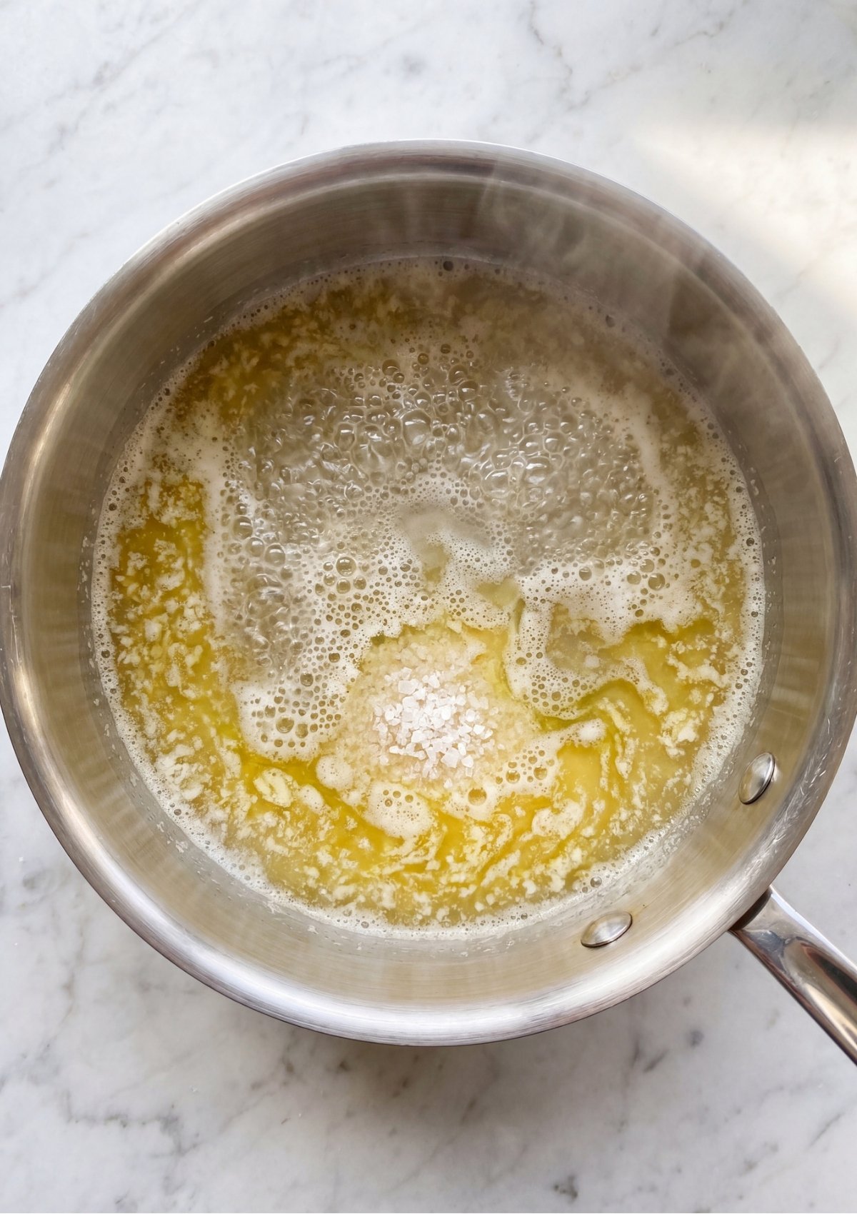 Water, butter, and salt reach a rolling boil and form bubbles in a metal saucepan, a crucial step for making the batter in this Patriotic Éclairs Recipe for July 4th Desserts.