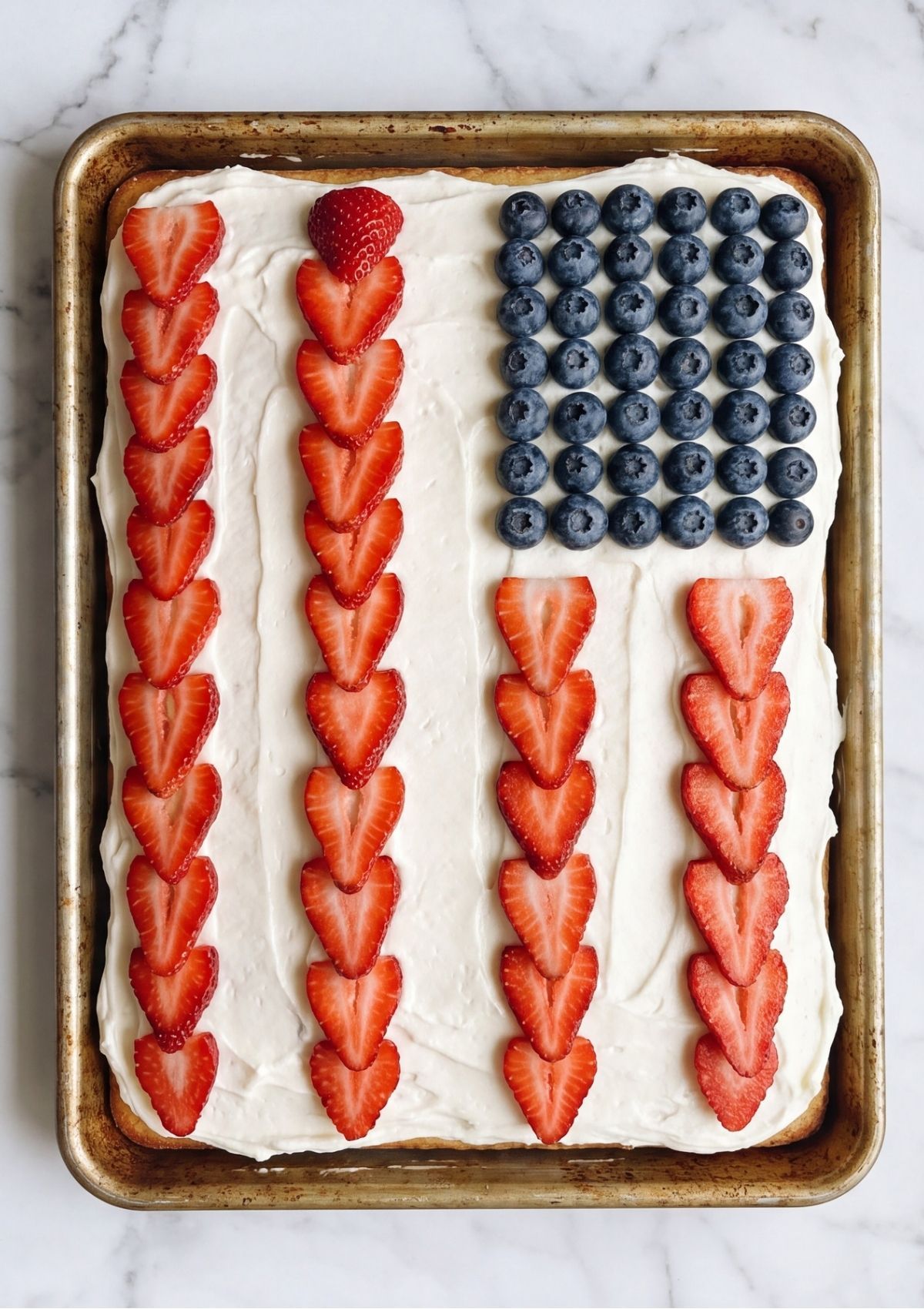 Overhead view of a sheet cake in a pan with blueberries and strawberries arranged to look like the stars and stripes.