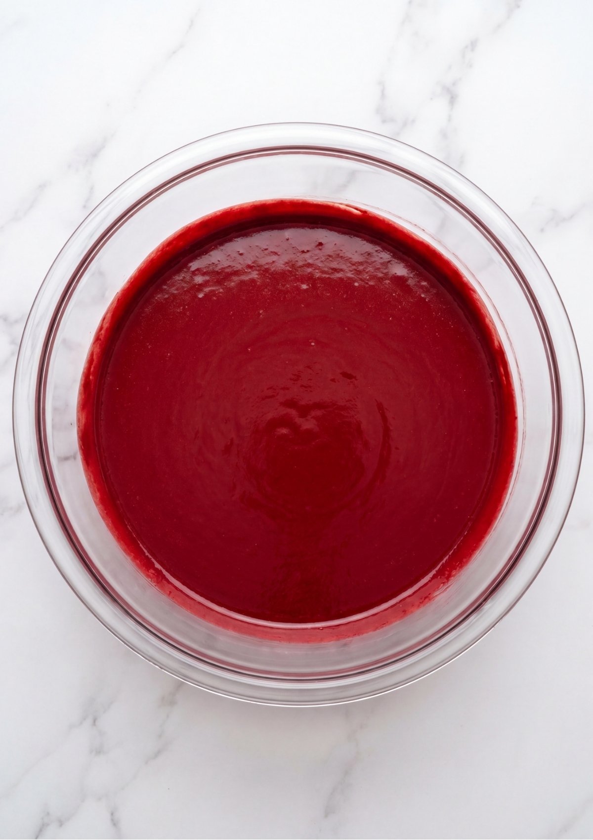 A glass bowl filled with smooth, deep red velvet cake batter, ready to be scooped into the muffin tin.