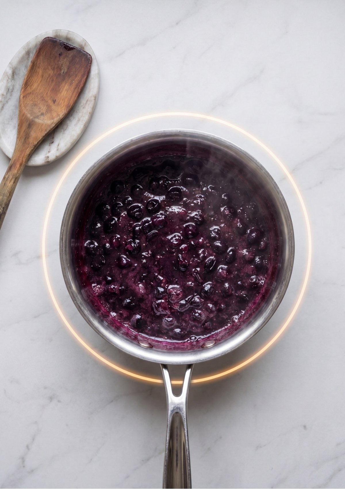 A stainless steel saucepan on a glowing burner filled with bubbling, dark purple blueberries cooking down into a thick sauce.