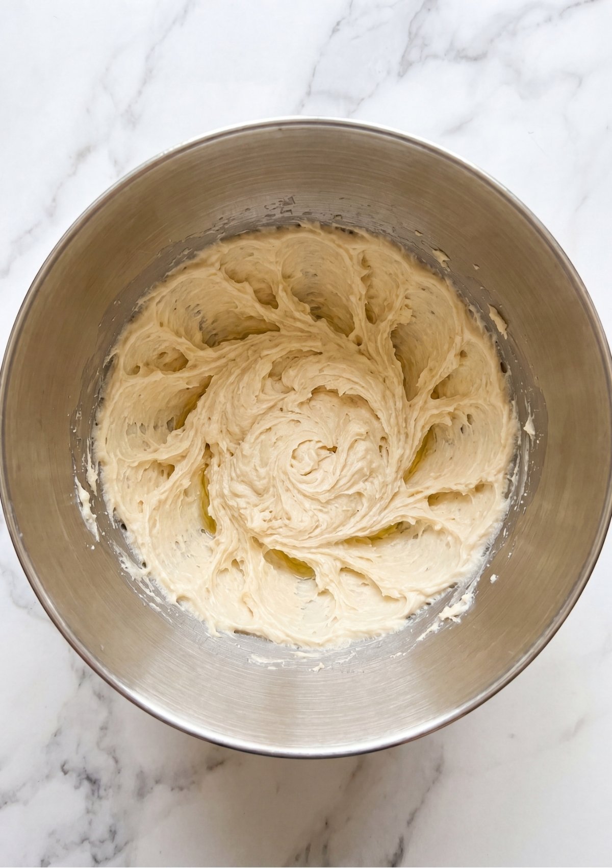 Creamy cookie dough mixture showing textured swirl patterns inside a large stainless steel mixing bowl