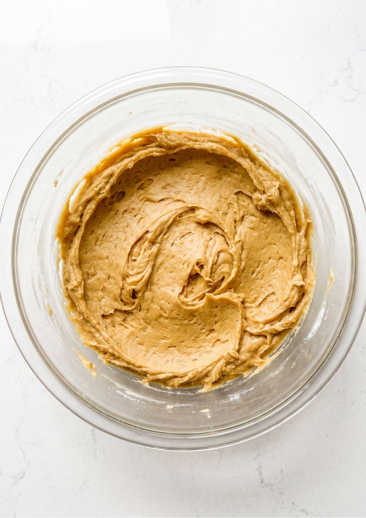Thick smooth golden brown cookie dough base mixed inside a clear glass bowl