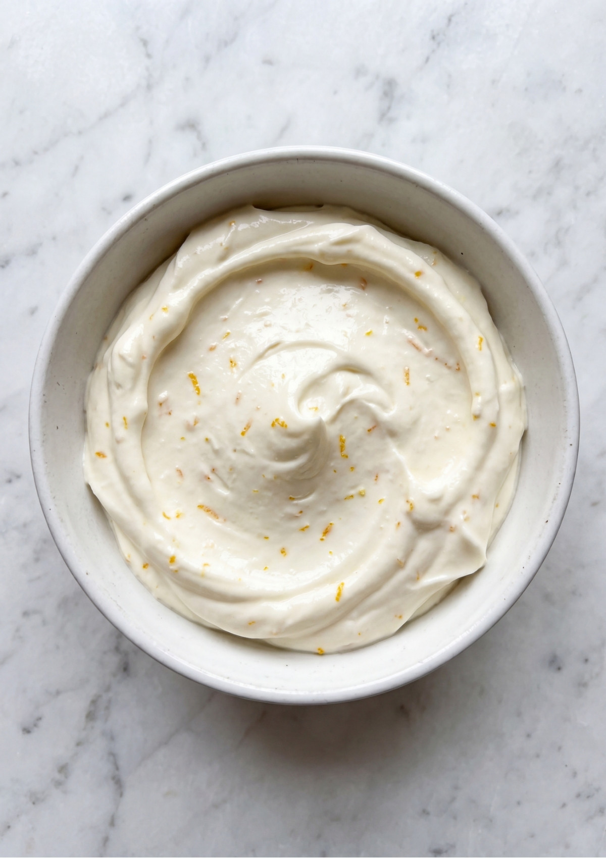 A white bowl filled with a thick, velvety cream base speckled with fresh yellow lemon zest, a key component for Patriotic Tartlets Recipe for Summer Parties.
