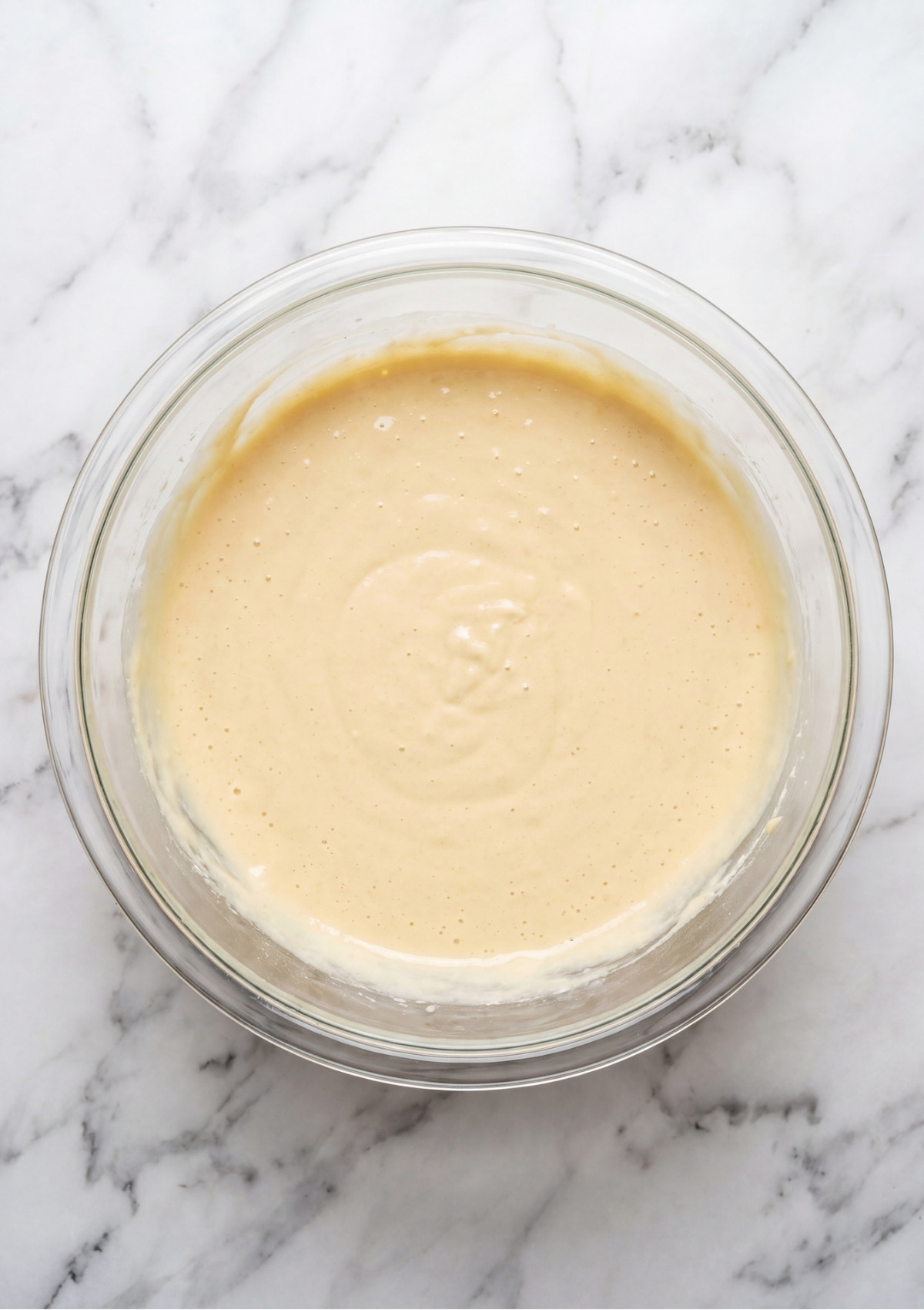 A close up view of a glass bowl filled with smooth, creamy cake batter ready for the oven.