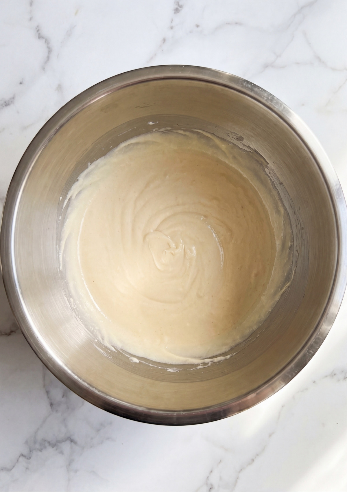 Smooth and pale cookie dough batter blended together in a silver stainless steel bowl on a white marble countertop