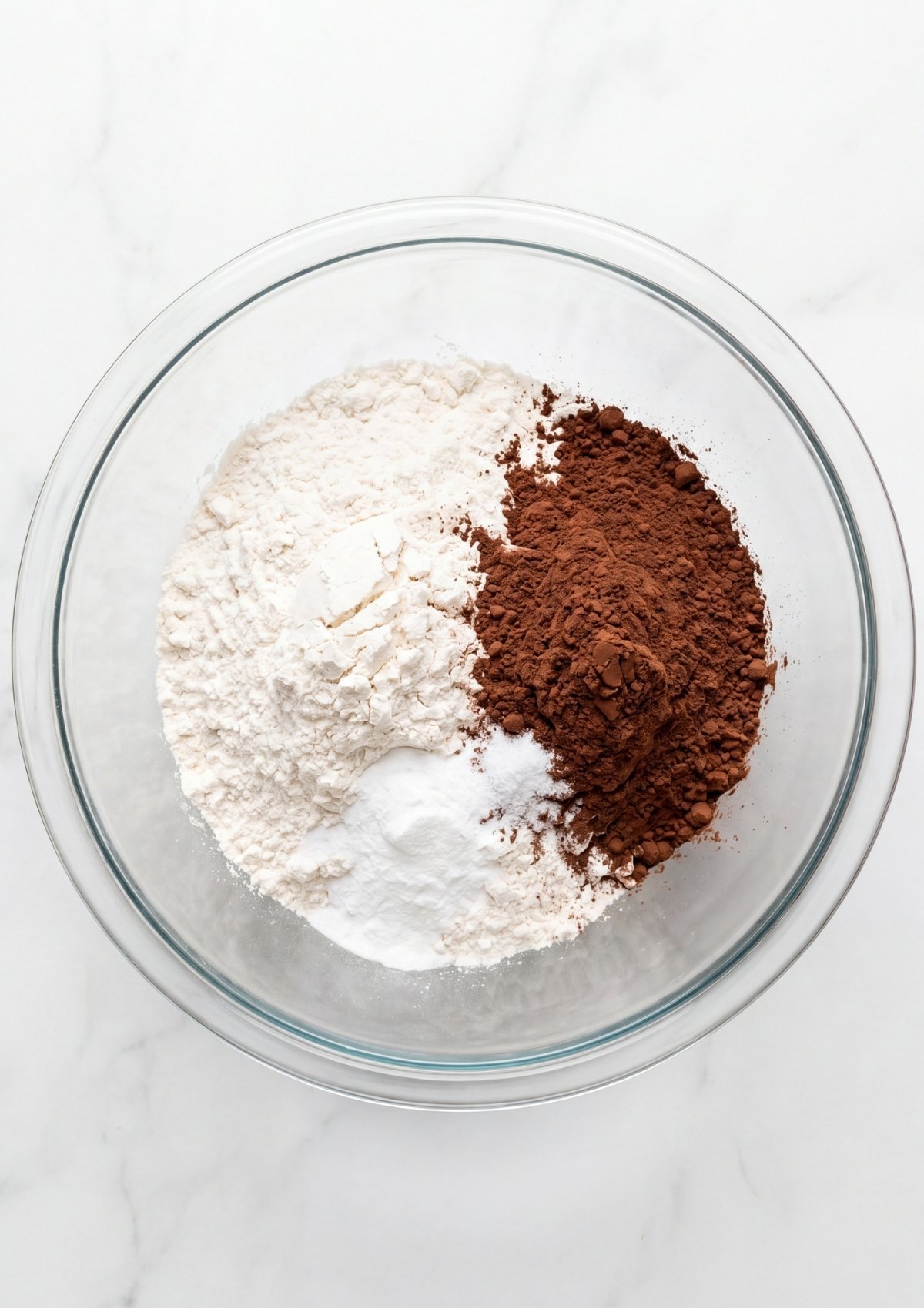 All purpose flour, unsweetened cocoa powder, baking soda, and salt unmixed in a clear glass bowl.