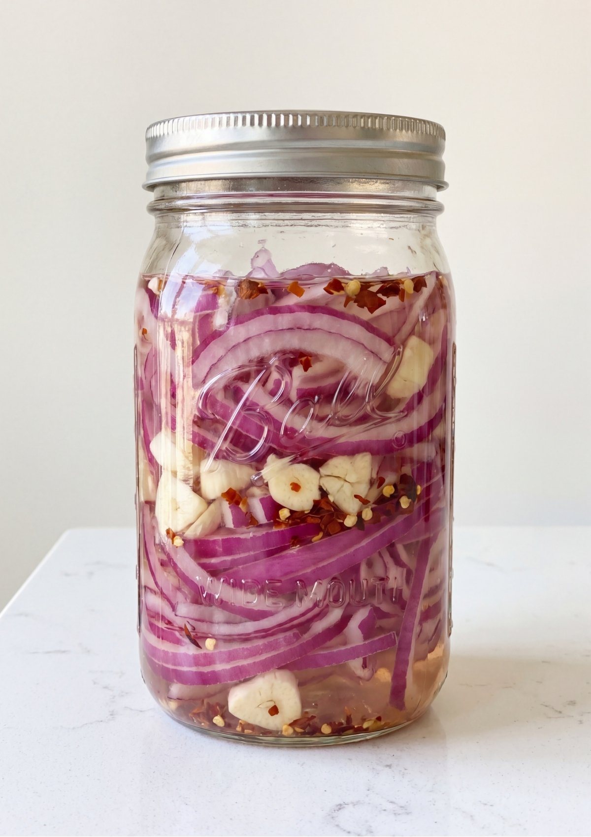 Sliced red onions and garlic submerged in liquid brine inside a sealed glass mason jar