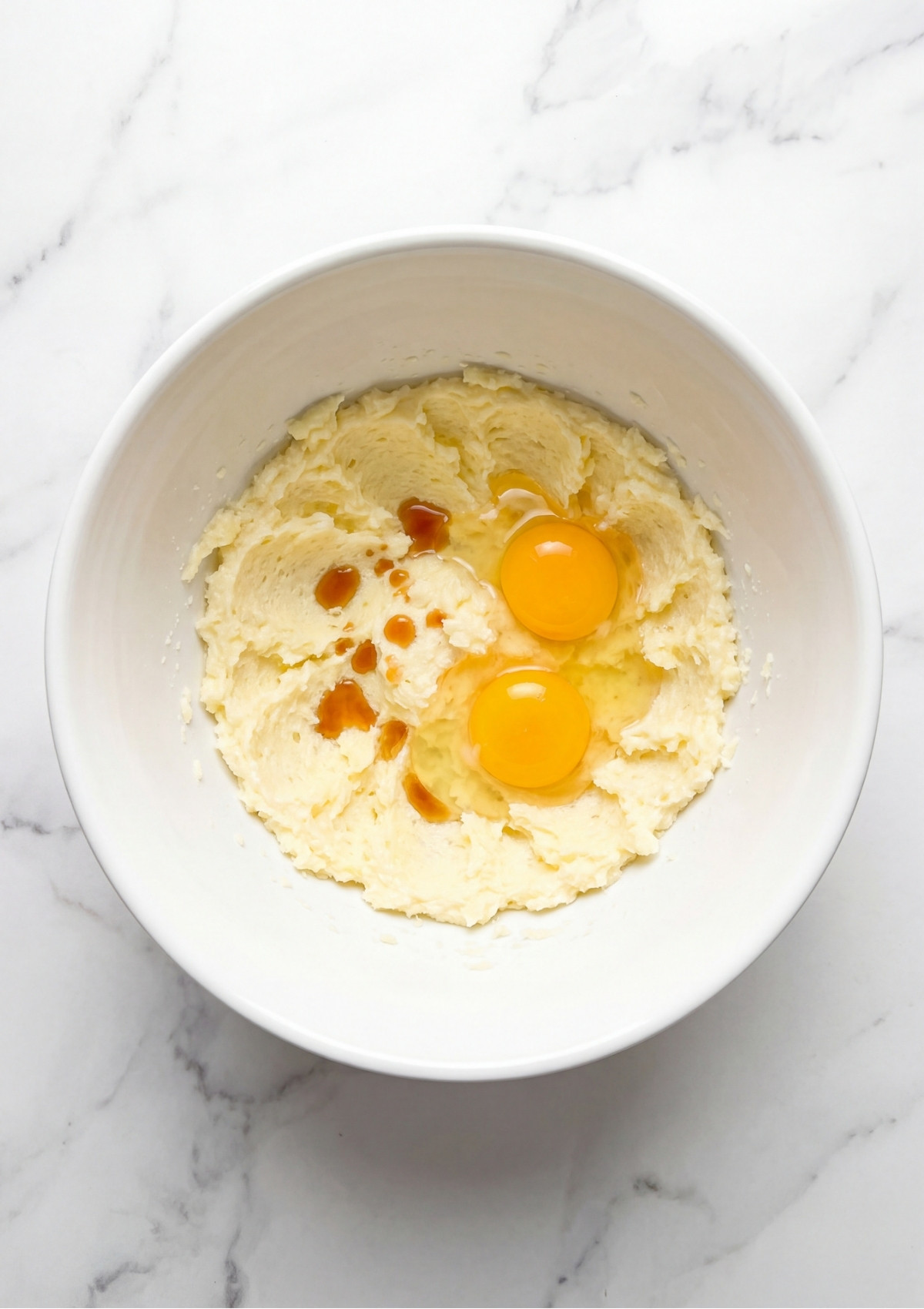 Two raw egg yolks and vanilla extract added to a bowl of creamed butter and sugar