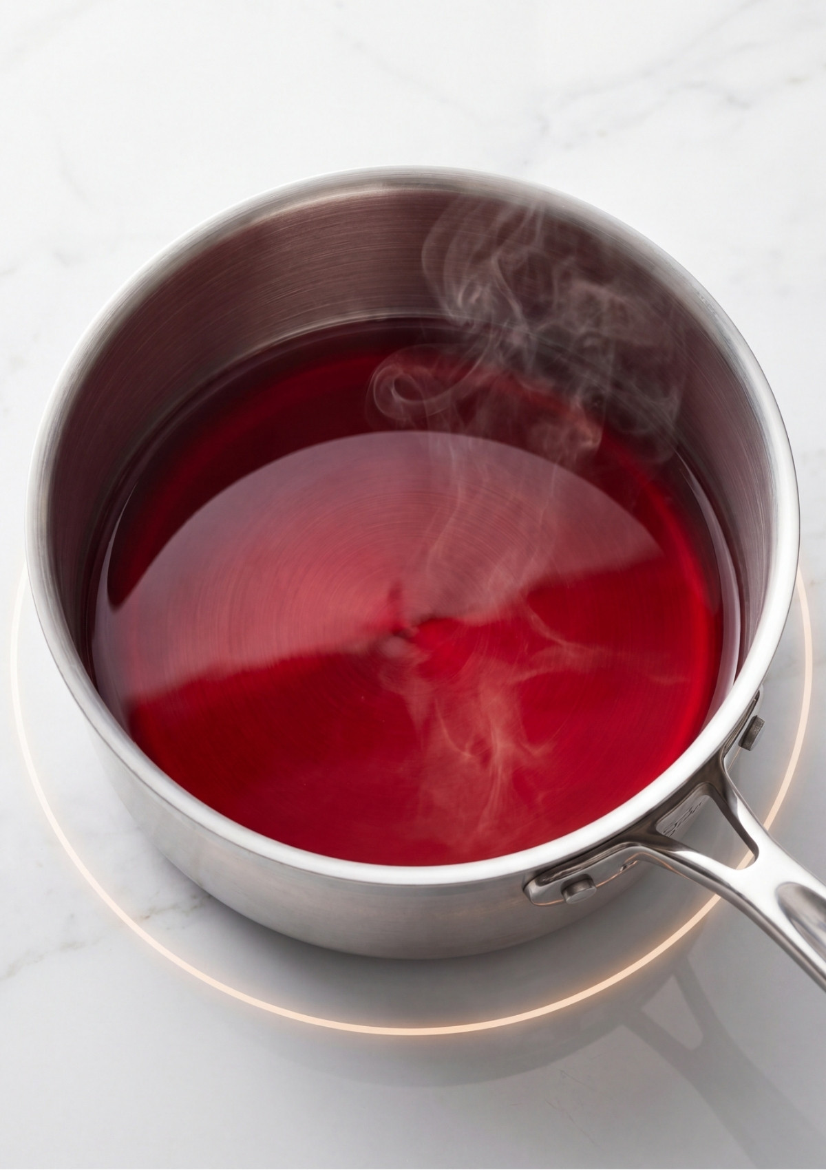 Steaming hot red liquid gelatin base fully dissolved in a stainless steel pot on an induction cooktop