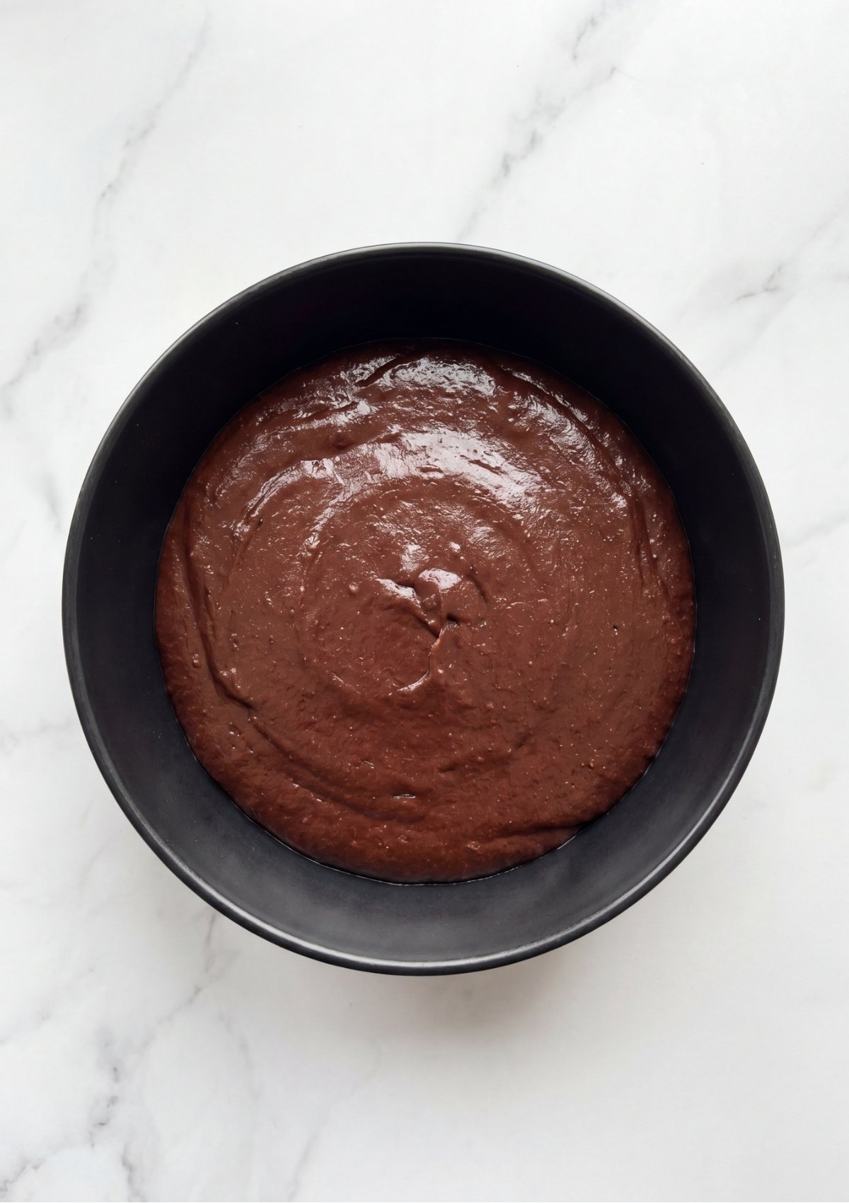 A perfectly smooth and glossy dark chocolate truffle batter spread into a black bowl before chilling.