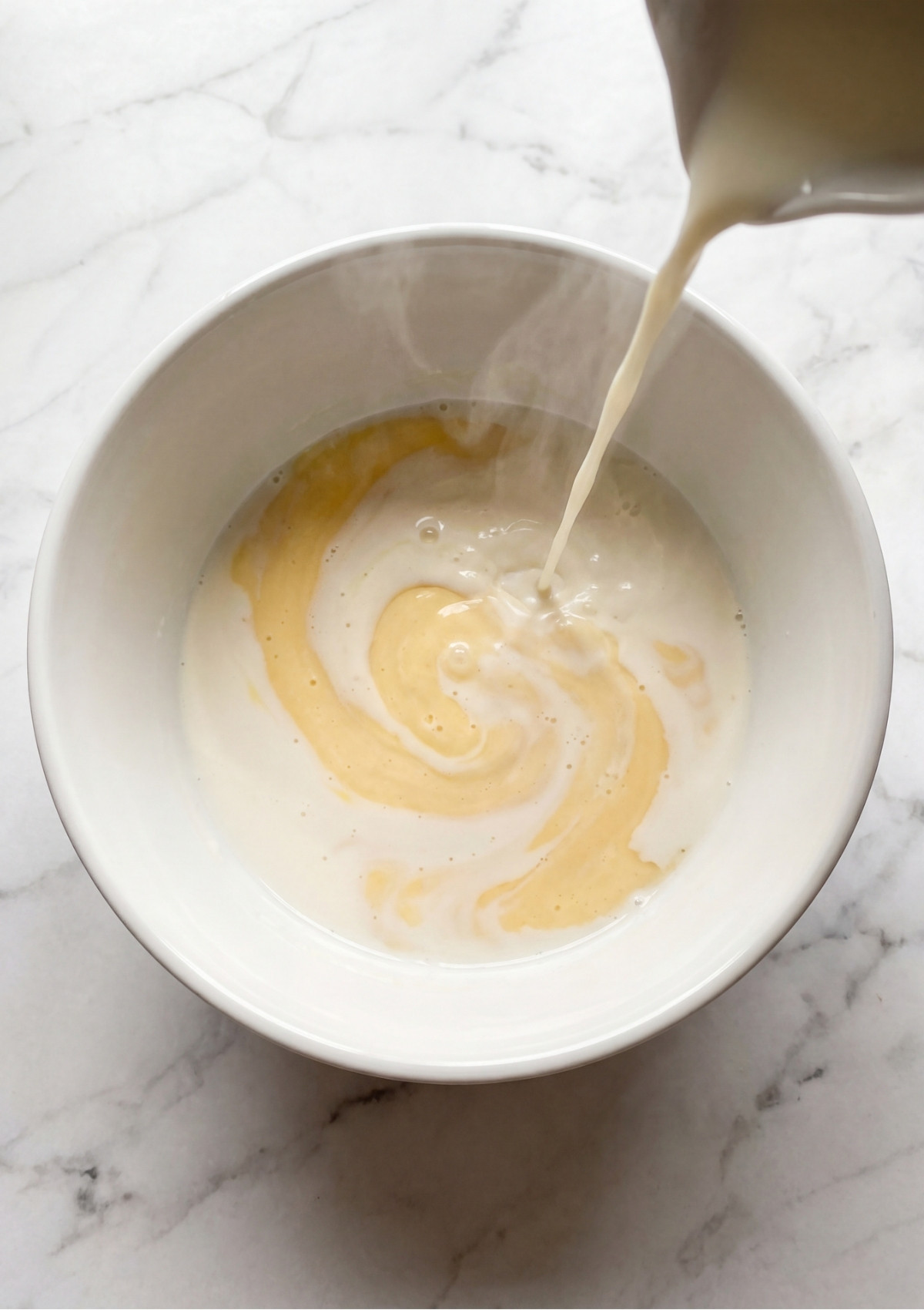 Warm milk being poured into a white bowl to begin the base for the éclair pastry cream.