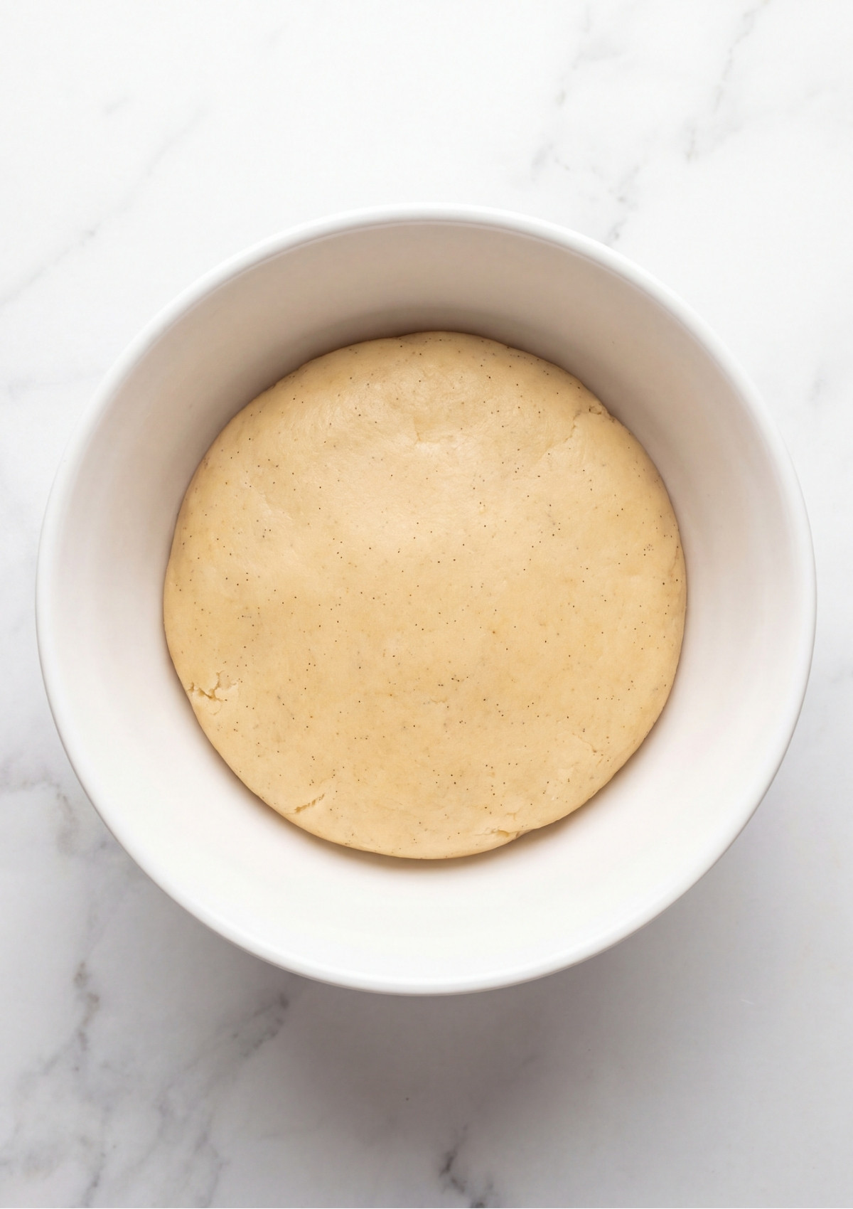 A white bowl containing a smooth ball of finished sugar cookie dough ready to be scooped