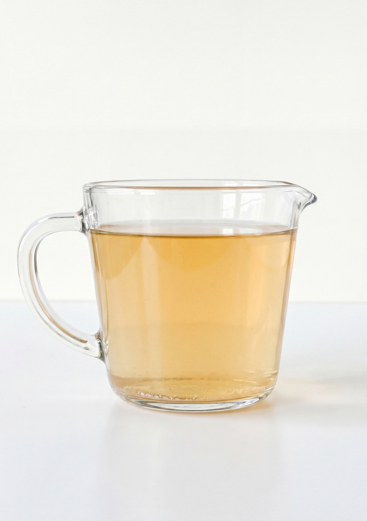 A clear glass measuring pitcher filled with a light amber vinegar and lemon juice brine against a white background