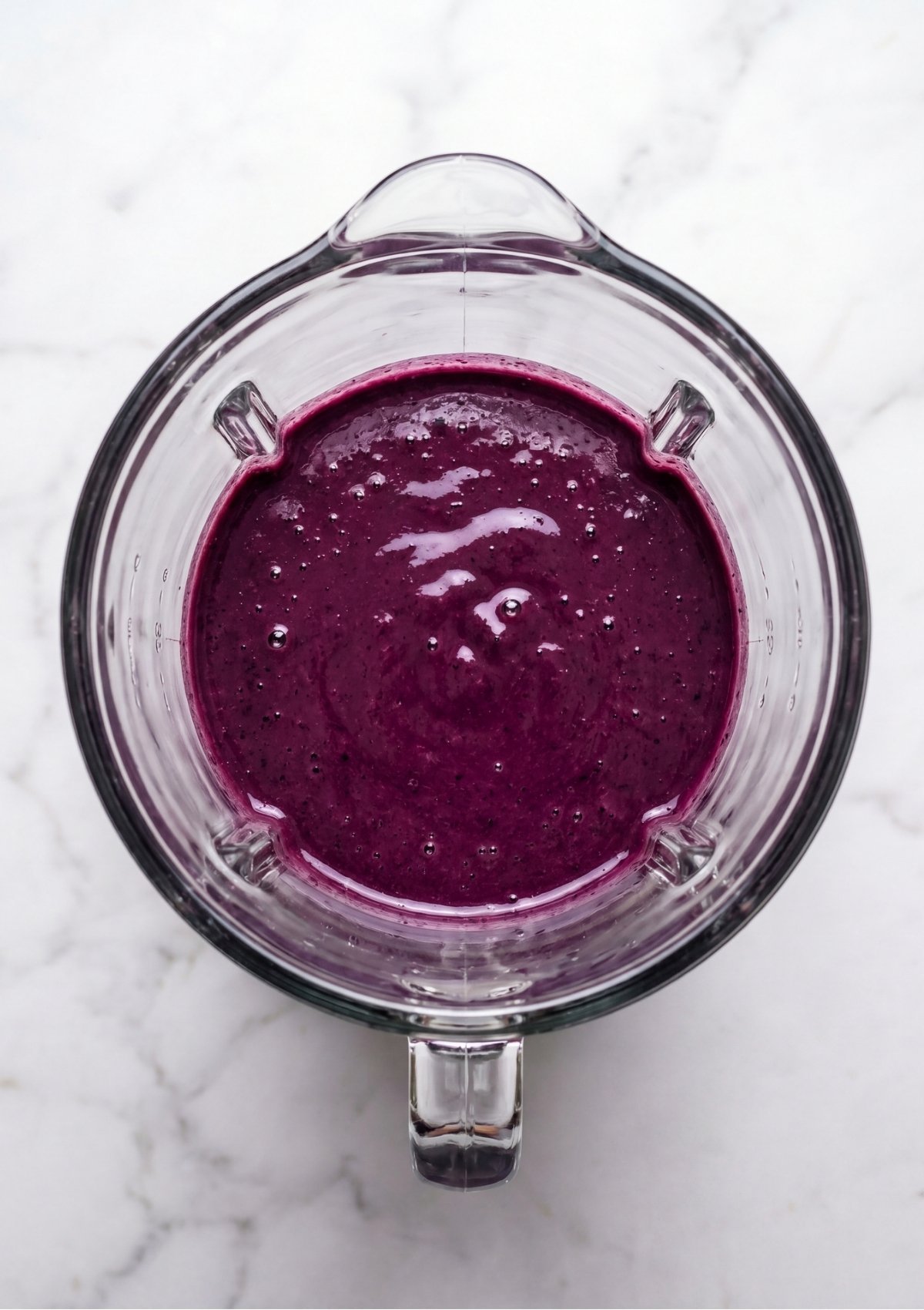 A top-down view of a glass blender filled with a smooth, vibrant purple blueberry puree for a Patriotic Red Velvet Cupcakes Recipe.