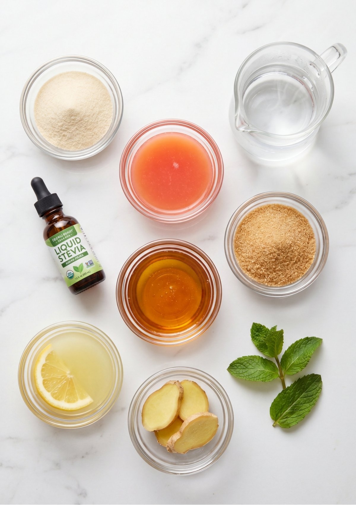 An overhead view of ingredients for a pink jello weight loss recipe, including bowls of gelatin powder, pink grapefruit juice, water, honey, brown sweetener, liquid stevia, lemon juice, sliced ginger, and mint leaves.