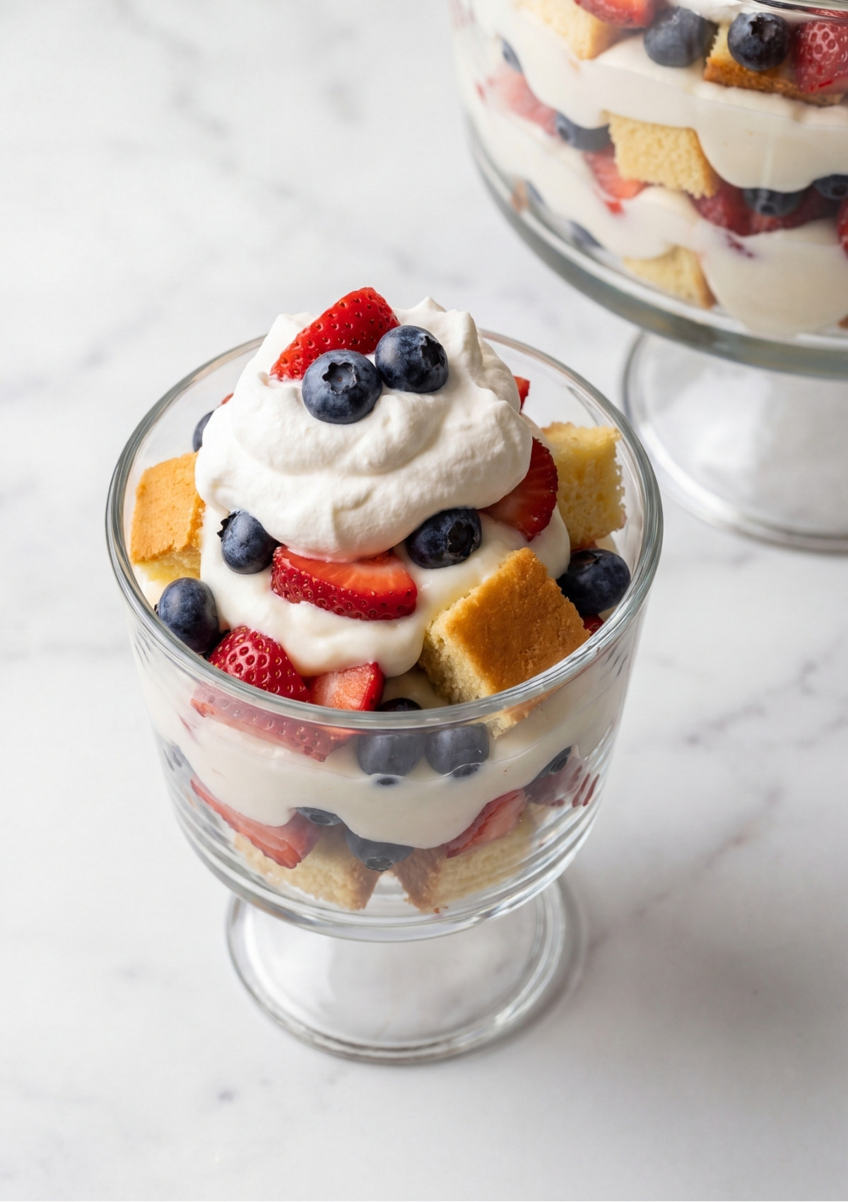 A small glass dish filled with layers of pound cake, cream, and berries topped with a dollop of whipped cream and fruit.