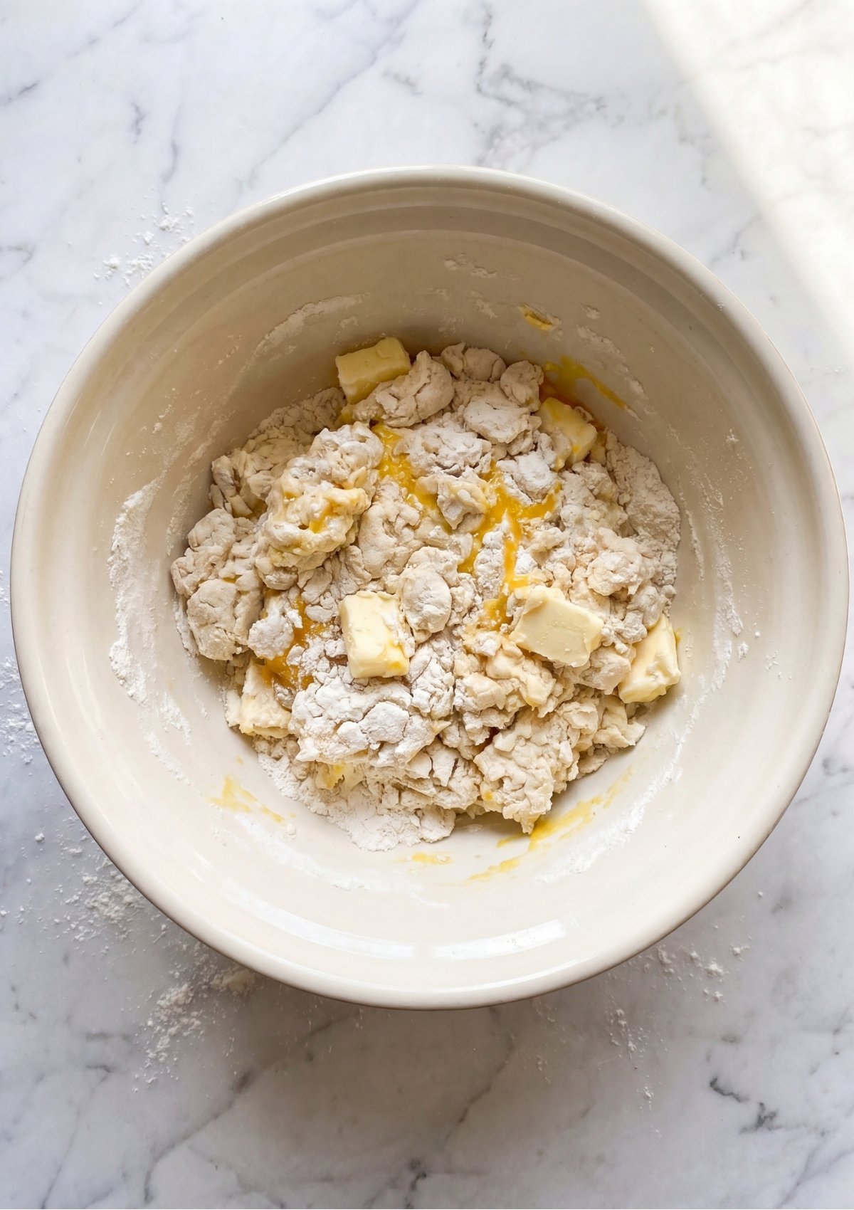 A large ceramic mixing bowl containing a shaggy dough mixture of white flour, yellow egg yolk, and cubes of cold butter being prepared for a Patriotic Tartlets Recipe for Summer Parties.