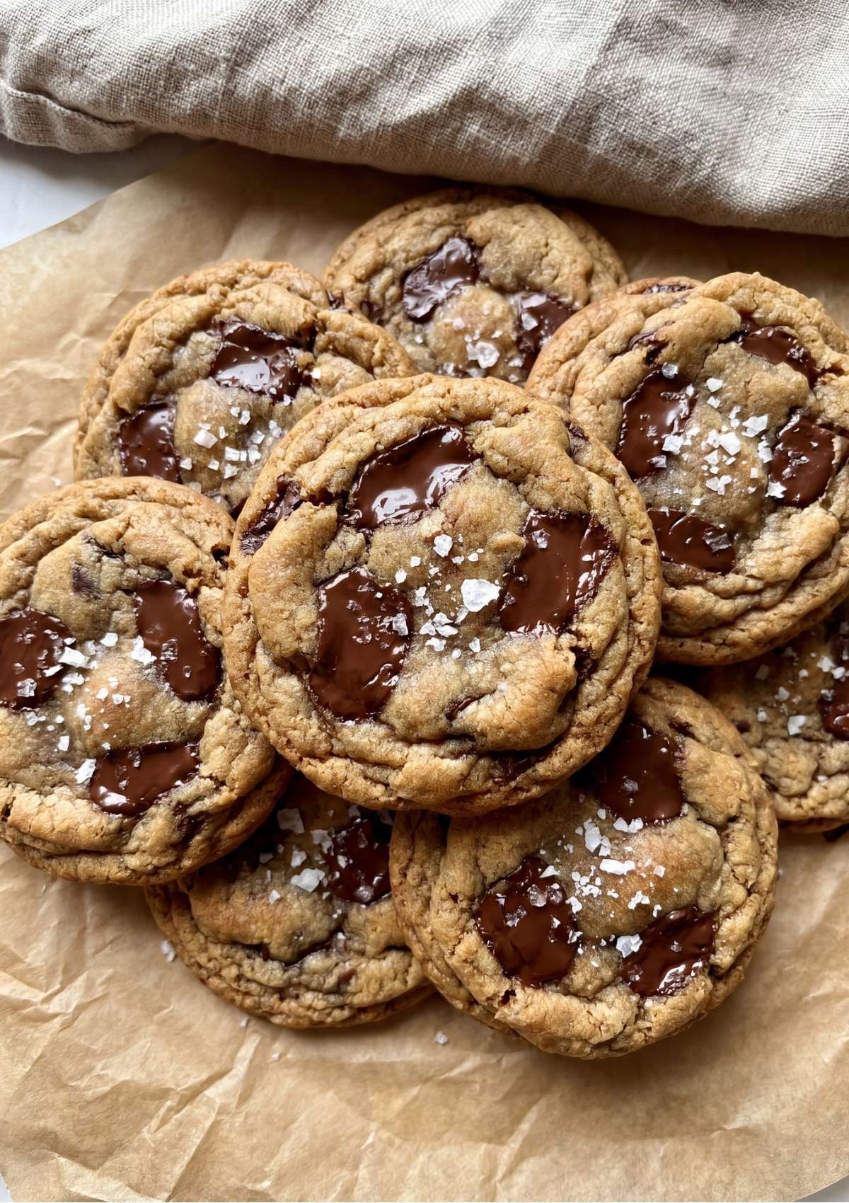 A close up pile of thick golden brown chocolate chunk cookies topped with melted chocolate puddles and coarse flaky sea salt