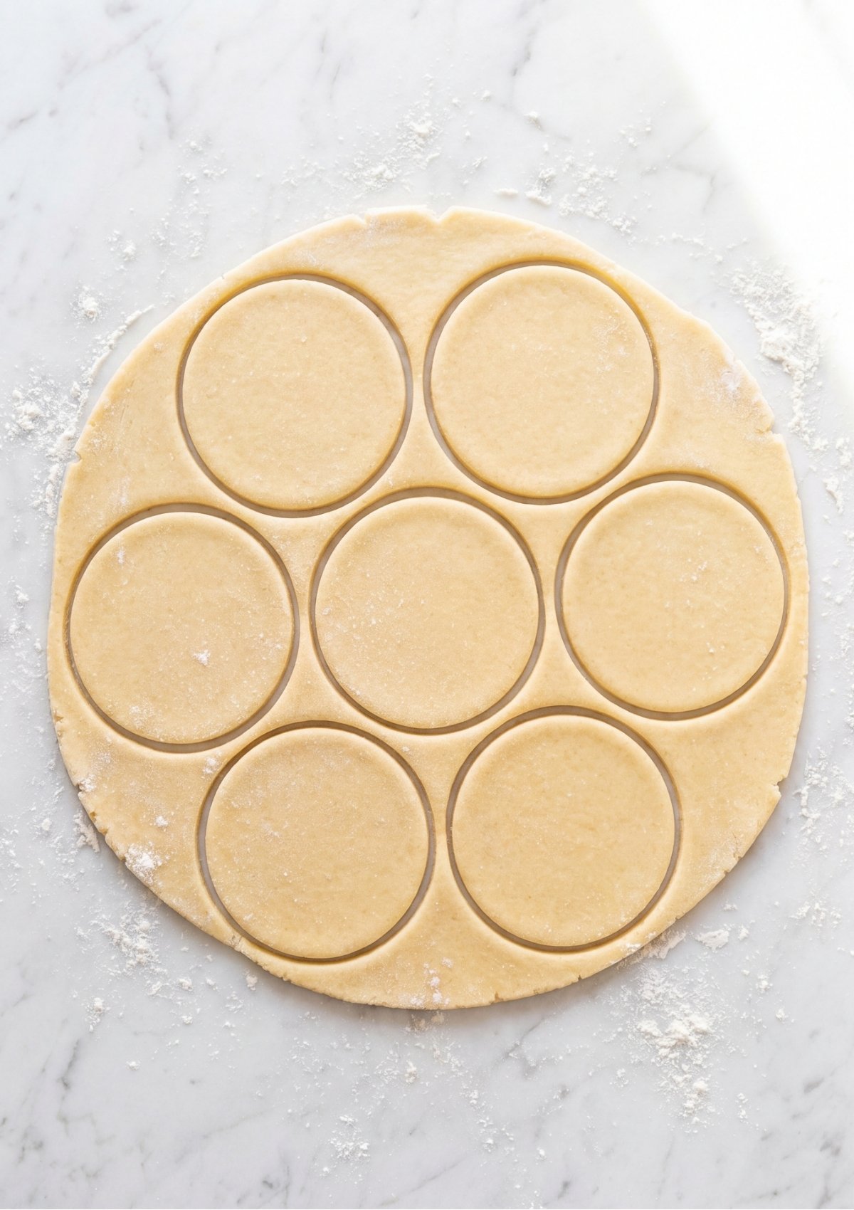 A sheet of flattened light-colored pastry dough on a marble surface with seven circular rounds cut out, ready to be baked for a Patriotic Tartlets Recipe for Summer Parties.