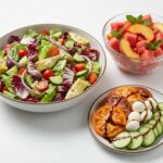 An assortment of fresh dishes including an Italian chopped salad, a watermelon peach salad, and a cucumber caprese plate.